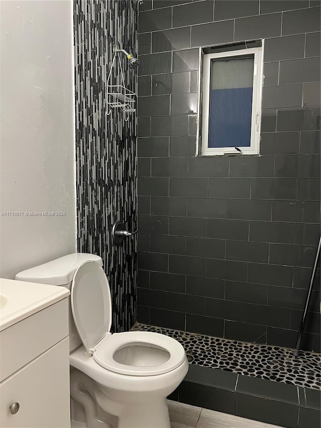 bathroom with tiled shower, tile patterned floors, vanity, and toilet