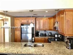 kitchen featuring light stone countertops, stainless steel fridge, black stove, sink, and hanging light fixtures