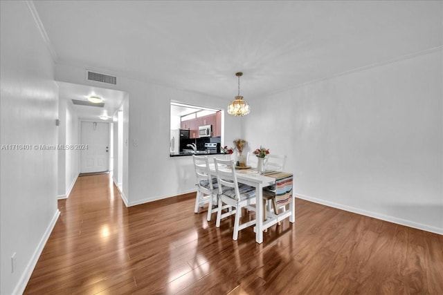 dining area with wood-type flooring, crown molding, and an inviting chandelier