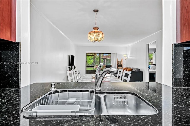 kitchen with sink, a notable chandelier, dark stone counters, pendant lighting, and ornamental molding