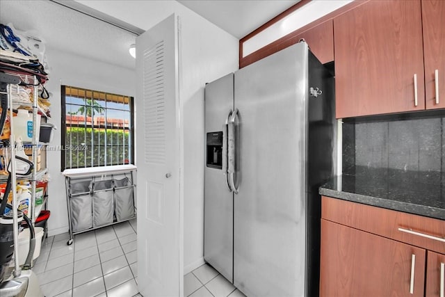 kitchen featuring stainless steel fridge with ice dispenser, dark stone counters, and light tile patterned flooring