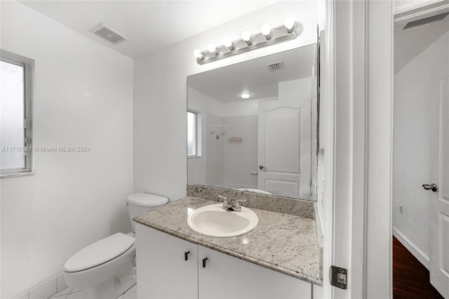 bathroom featuring toilet, vanity, wood-type flooring, and tiled shower