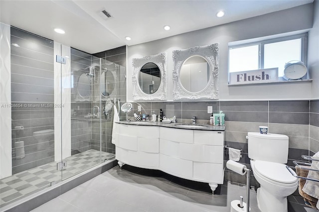 bathroom with tile patterned floors, toilet, a shower with shower door, and tile walls