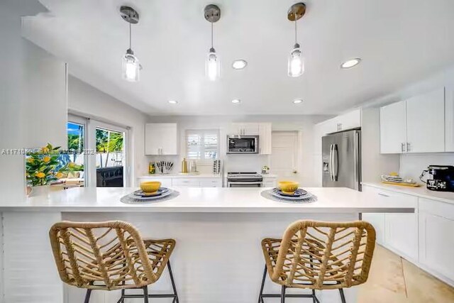 kitchen featuring a kitchen bar, appliances with stainless steel finishes, white cabinetry, and pendant lighting