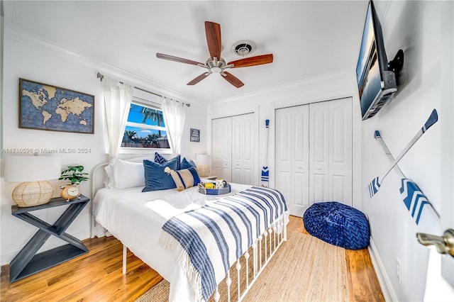 bedroom with two closets, hardwood / wood-style flooring, ceiling fan, and ornamental molding