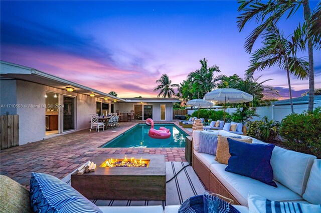 pool at dusk featuring an outdoor living space with a fire pit and a patio