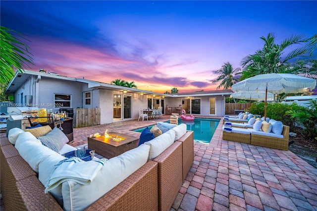 pool at dusk featuring a patio, a fire pit, and grilling area