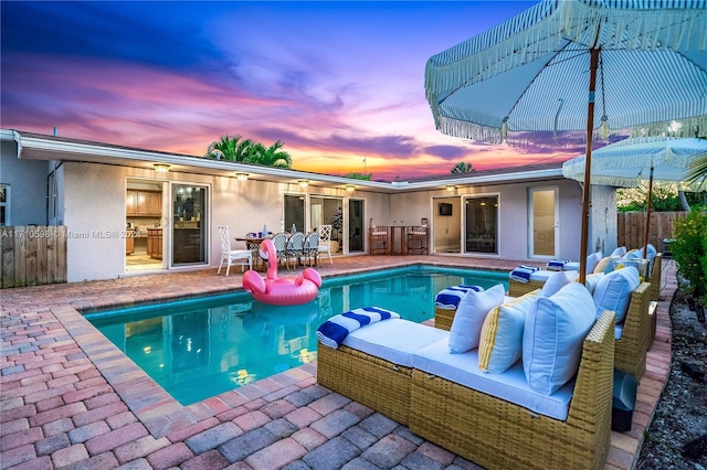 pool at dusk featuring a patio area and an outdoor living space