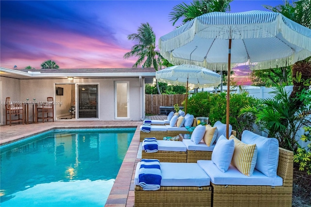 pool at dusk featuring outdoor lounge area and an outdoor bar