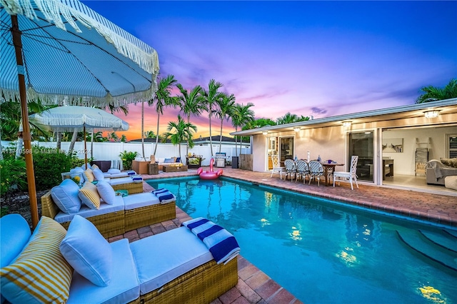 pool at dusk featuring an outdoor living space and a patio