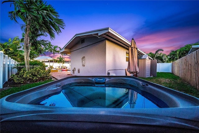 pool at dusk featuring a hot tub and a deck