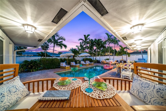 pool at dusk with outdoor lounge area and a patio area