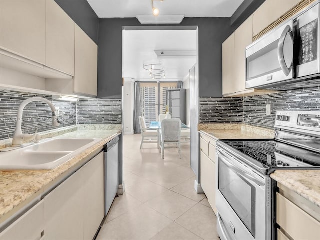 kitchen featuring backsplash, stainless steel appliances, sink, light tile patterned floors, and cream cabinetry