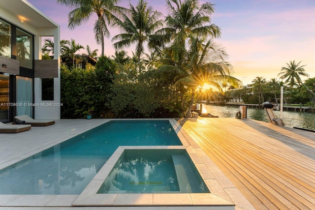 pool at dusk featuring a water view and a patio