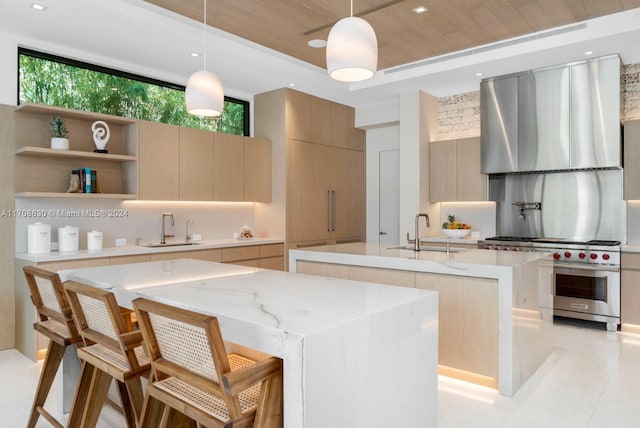 kitchen with luxury range, a kitchen island with sink, sink, decorative light fixtures, and wall chimney exhaust hood