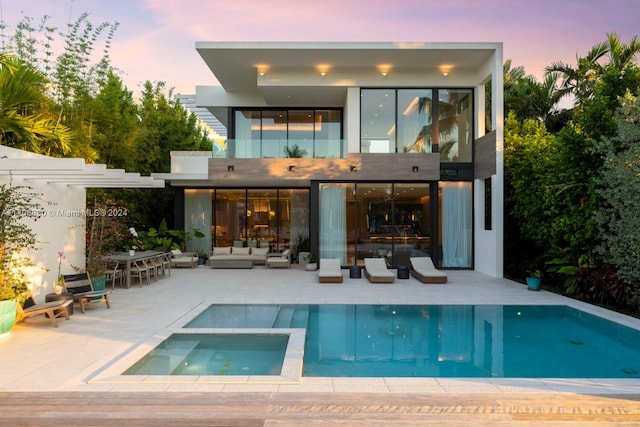 back house at dusk featuring a pool with hot tub, an outdoor hangout area, and a patio