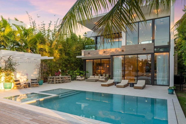 pool at dusk featuring an in ground hot tub, a patio area, and an outdoor living space