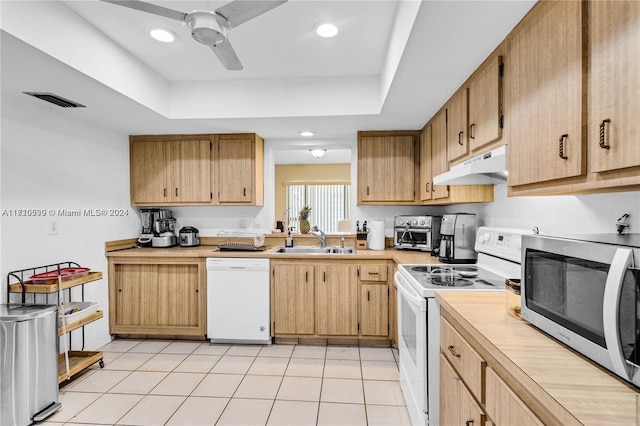 kitchen with ceiling fan, sink, white appliances, a tray ceiling, and light tile patterned floors