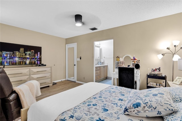 bedroom with a textured ceiling, ensuite bathroom, ceiling fan, and light hardwood / wood-style floors