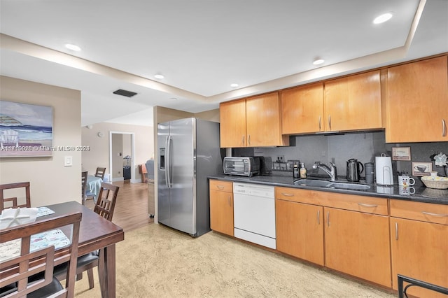 kitchen featuring dishwasher, sink, tasteful backsplash, stainless steel refrigerator with ice dispenser, and dark stone countertops