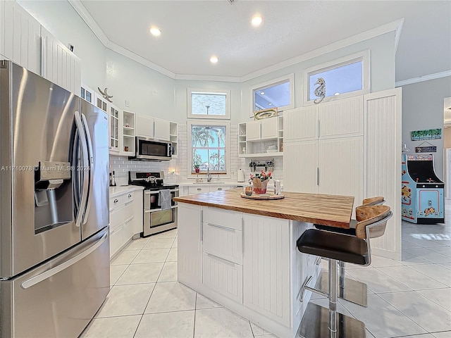 kitchen with light tile patterned floors, butcher block countertops, crown molding, white cabinets, and appliances with stainless steel finishes