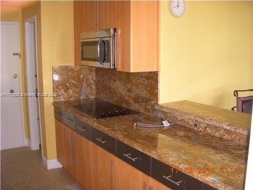 kitchen with tile patterned flooring, backsplash, black electric cooktop, and light stone counters