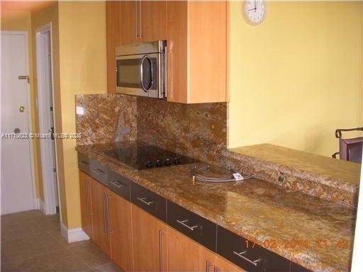 kitchen with tasteful backsplash, light stone counters, light tile patterned floors, black electric stovetop, and stainless steel microwave