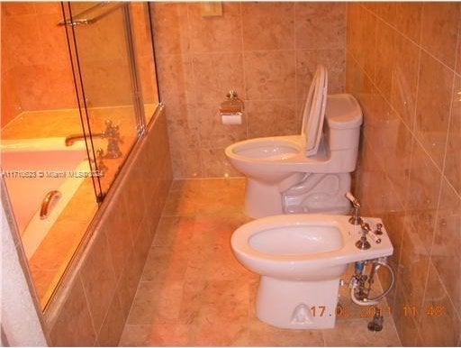 bathroom featuring tile patterned flooring, enclosed tub / shower combo, and tile walls