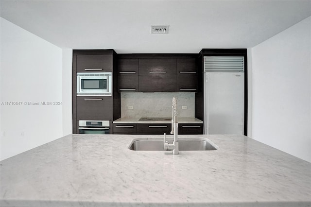 kitchen featuring backsplash, sink, built in appliances, dark brown cabinets, and light stone counters