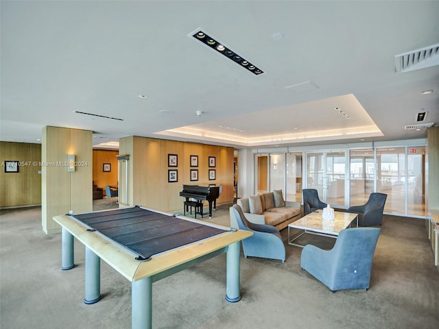 recreation room with carpet, a tray ceiling, and wood walls