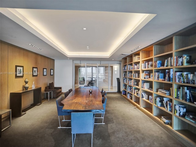 dining area with dark carpet, a tray ceiling, and wood walls