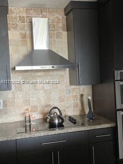 kitchen with wall chimney exhaust hood, oven, light stone countertops, and tasteful backsplash