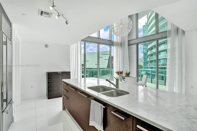 kitchen with dark brown cabinets, sink, light tile patterned floors, light stone counters, and a wall of windows