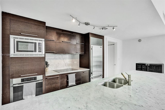 kitchen with built in appliances, dark brown cabinetry, light stone countertops, and sink