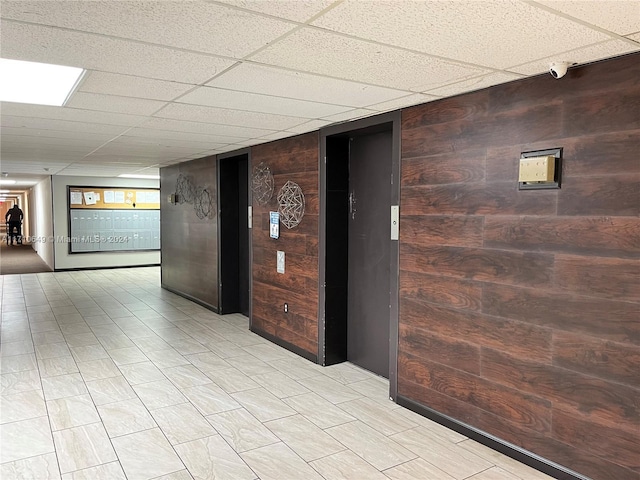 corridor with elevator, wooden walls, and a drop ceiling