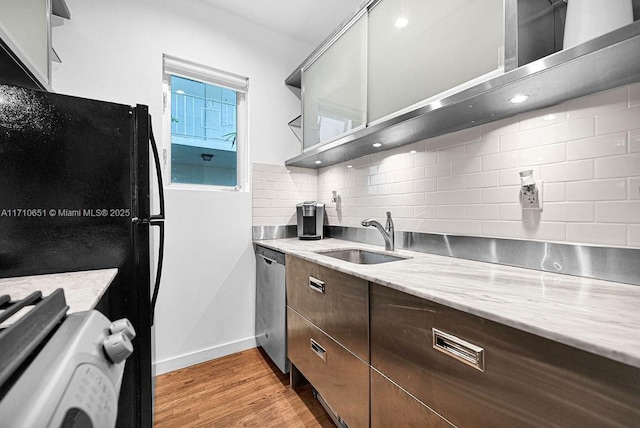 kitchen featuring light stone countertops, dishwasher, sink, light hardwood / wood-style floors, and decorative backsplash