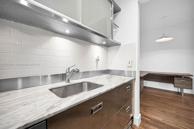 kitchen with sink, dark wood-type flooring, light stone counters, backsplash, and pendant lighting