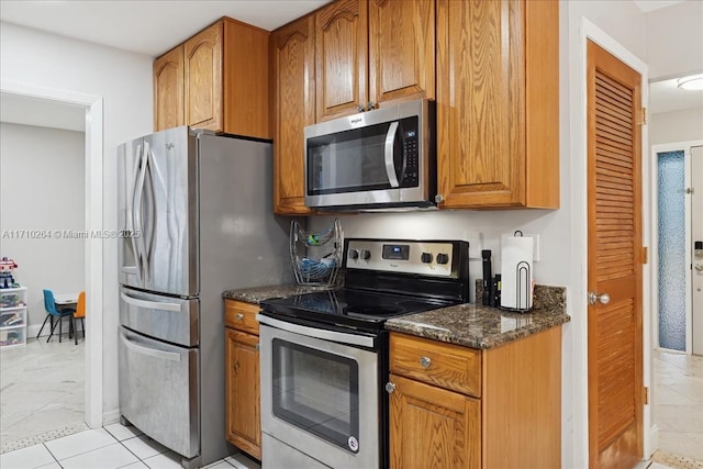 kitchen featuring stainless steel appliances, dark stone counters, and light tile patterned floors