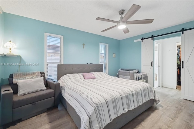 bedroom featuring ceiling fan, a barn door, and wood-type flooring