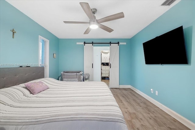 bedroom with ceiling fan, light hardwood / wood-style floors, and a barn door