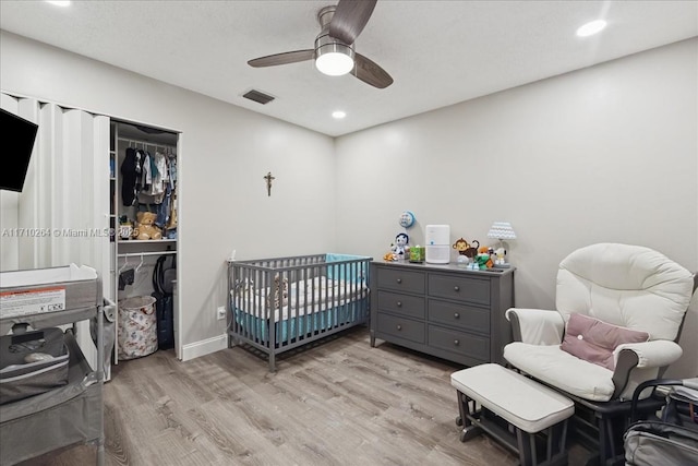 bedroom with ceiling fan, a crib, a closet, and light hardwood / wood-style flooring