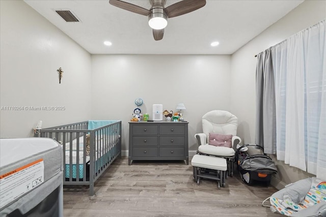 bedroom featuring ceiling fan, light hardwood / wood-style flooring, and a crib