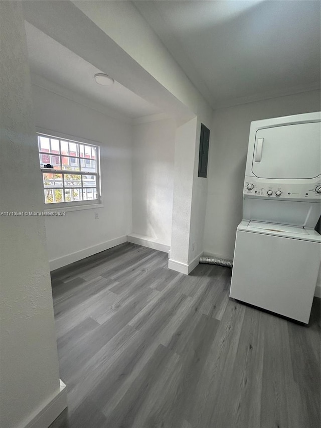 laundry room with electric panel, ornamental molding, stacked washing maching and dryer, and wood-type flooring