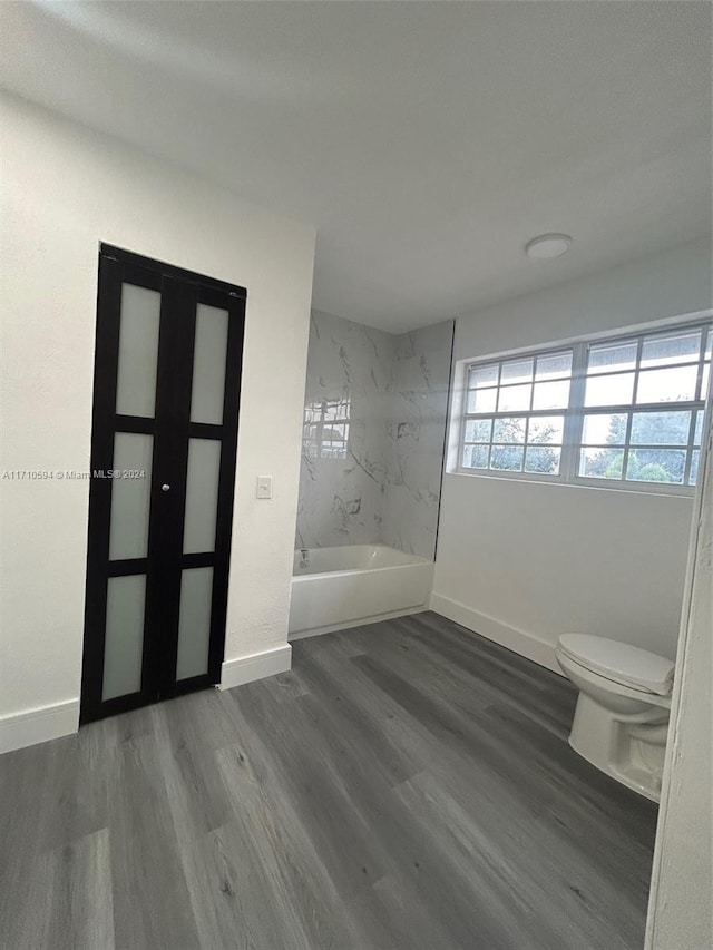 bathroom with hardwood / wood-style floors, tiled shower / bath combo, toilet, and french doors