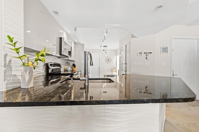 kitchen with kitchen peninsula, dark stone counters, stainless steel appliances, sink, and white cabinets