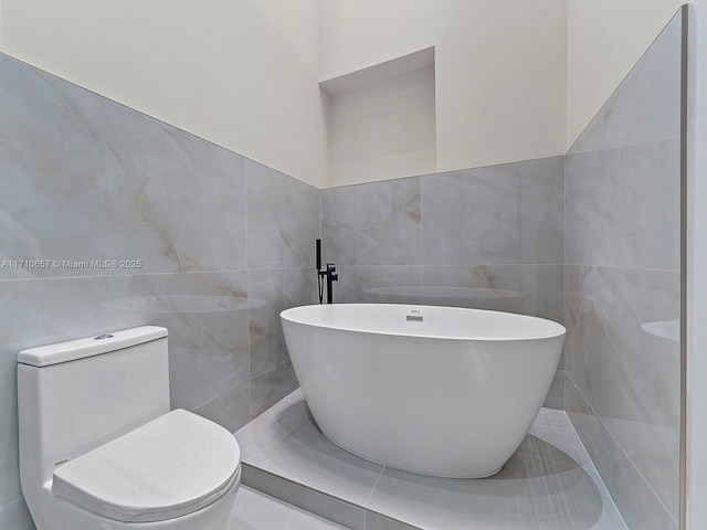 full bathroom with toilet, a freestanding tub, and tile walls