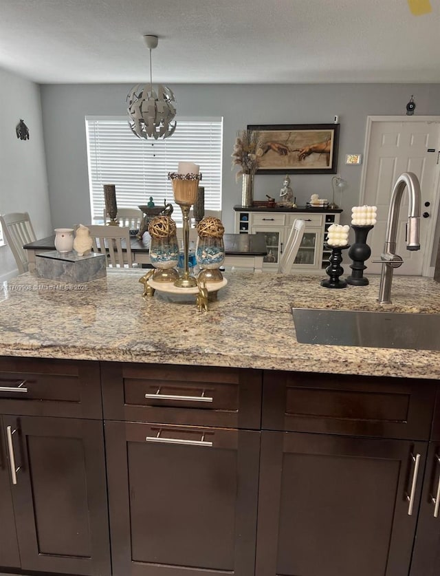 kitchen with light stone counters, dark brown cabinetry, decorative light fixtures, and sink