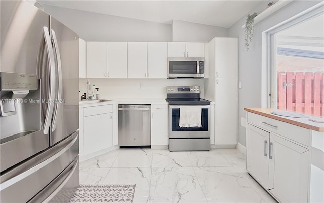 kitchen featuring stainless steel appliances, white cabinetry, lofted ceiling, and sink