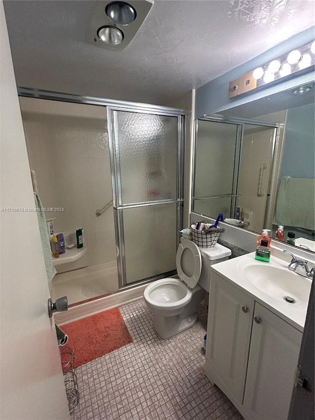 bathroom with tile patterned floors, vanity, an enclosed shower, and toilet