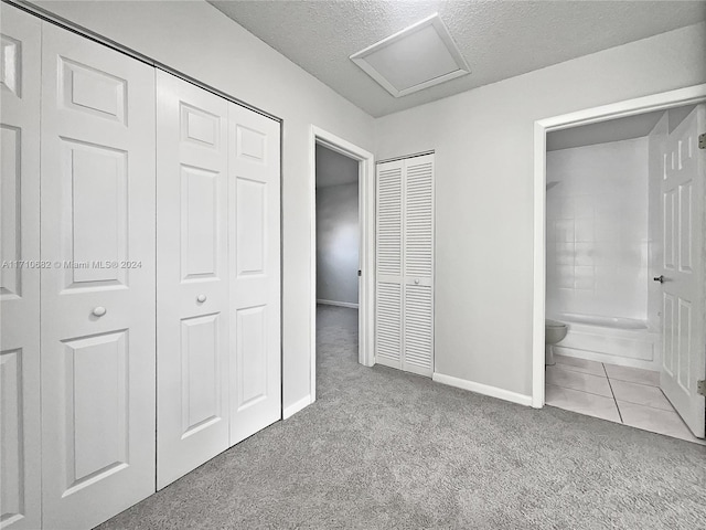 unfurnished bedroom featuring light colored carpet, a textured ceiling, connected bathroom, and multiple closets